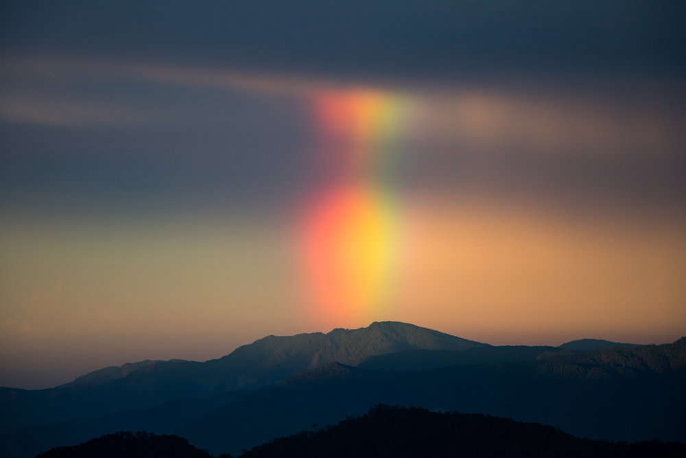 A massive rainbow descends over the mountains at sunset.
